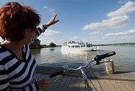 Eine Fahrradfahrerin grüßt die Passagiere der MS Altmühlsee vom Ufer aus