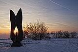 Kunstobjekt bei Sonnenaufgang am schneebedecktem Altmühlsee. Einige Meter dahinter stehen einige Sträucher.