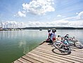 Zwei Rennradler machen Pause am Brombachsee. Sie sitzen dabei auf einem Holzsteg und blicken zu den Segelbooten