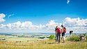Zwei Personen mit Rucksäcken stehen auf einem Hügel und blicken durch ein Fernglas auf eine weite Landschaft.