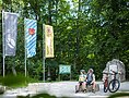 Zwei Radfahrer mit Helm sitzen auf Steinbank im Wald neben zwei Mountainbikes und drei Fahnen.